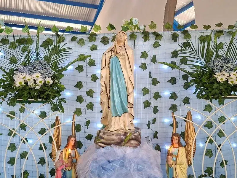 La advocación de la Virgen de Lourdes tiene su origen en Francia (1858), cuando la Virgen María se apareció a Santa Bernardita Soubirous en la gruta de Massabielle. Desde entonces, la imagen de la Virgen en una gruta se convirtió en símbolo de fe, esperanza y sanación.